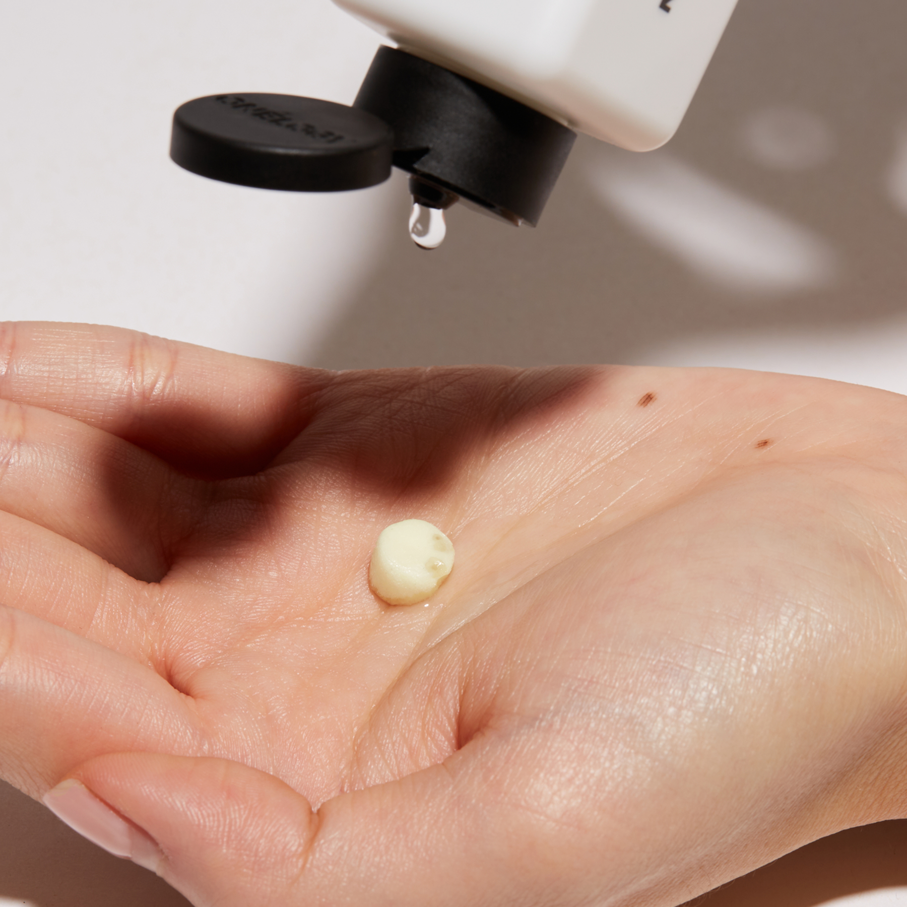 Hand holding a droplet of skincare product with a bottle in the background