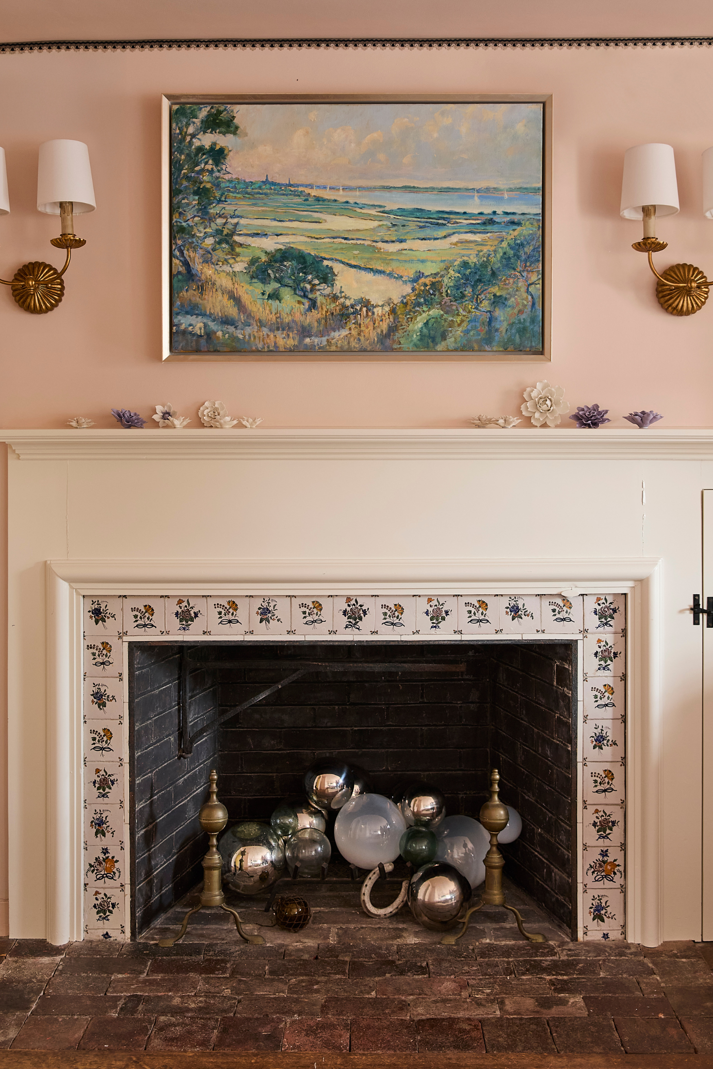 Decorative fireplace with ornate tiles and decorative objects, wall sconces, and a painting on the wall.