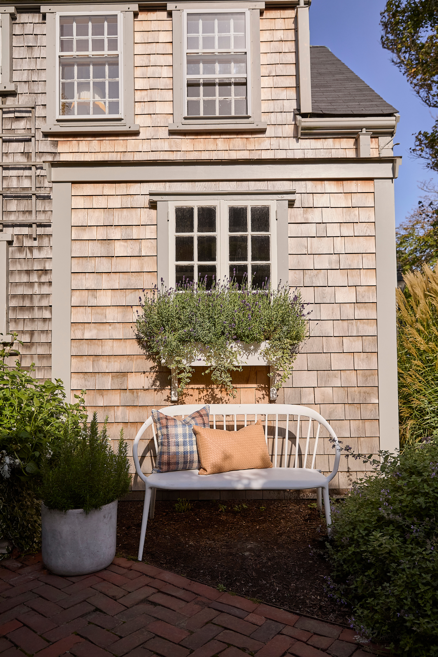 White bench with plaid and brown pillow against a wooden house with window boxes.