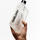 Hand holding a Oneleyology product bottle against a white background
