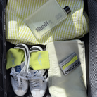 Open suitcase with yellow checkered towel, white sneakers, yellow socks, and grooming products.