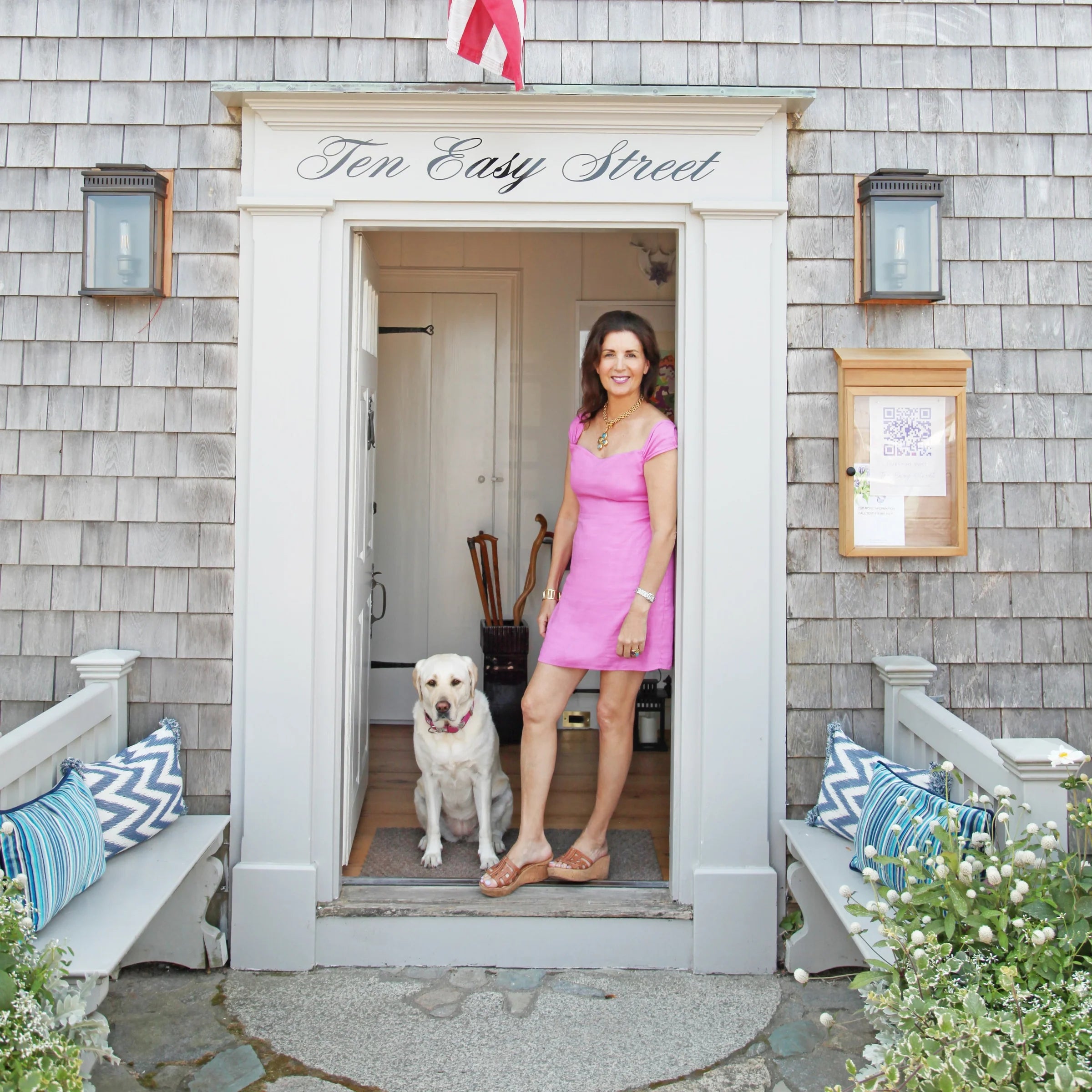 Woman in a pink dress standing in the doorway of a house with a dog by her side, surrounded by decorative elements.