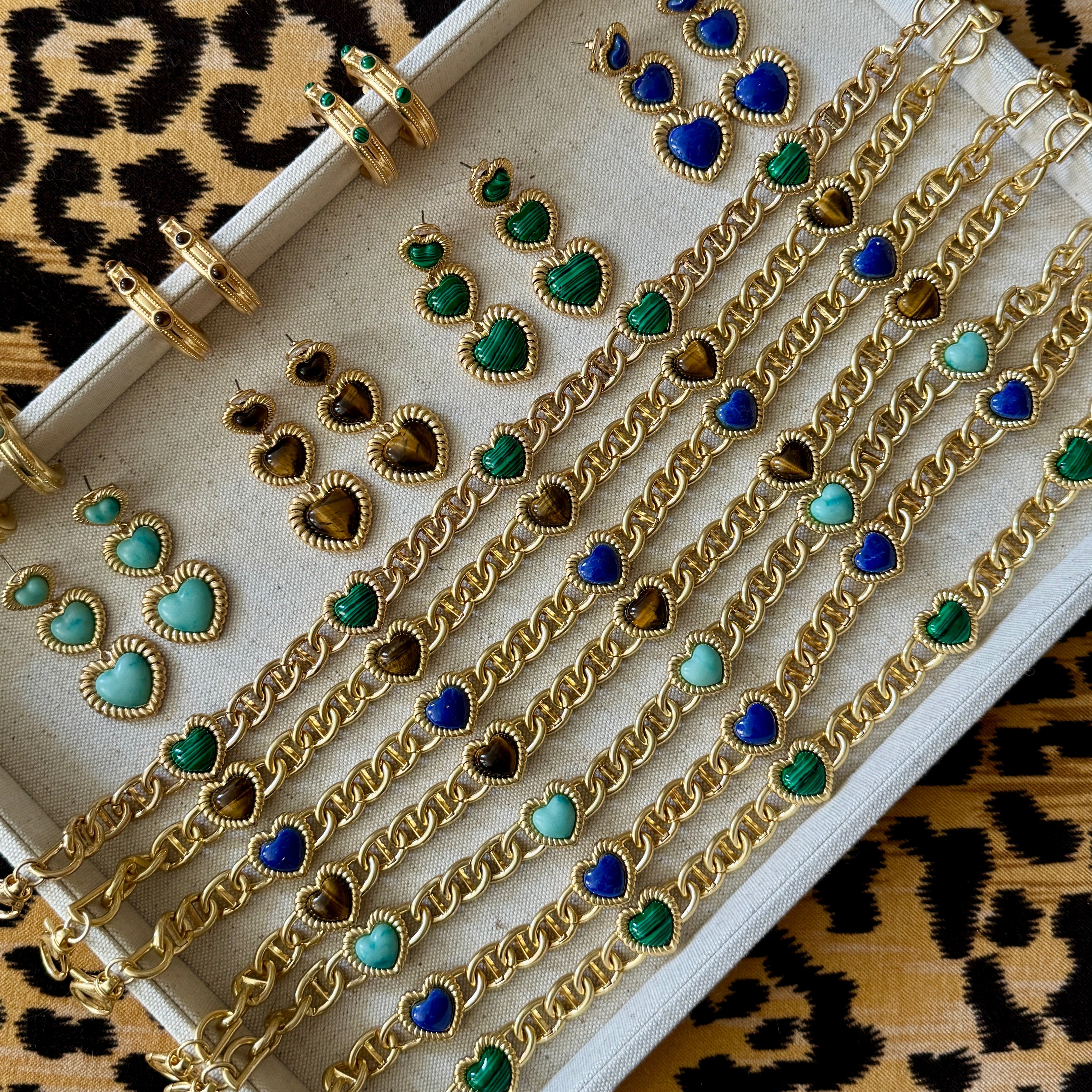 Gold jewelry set with green and blue heart-shaped stones on a leopard print background