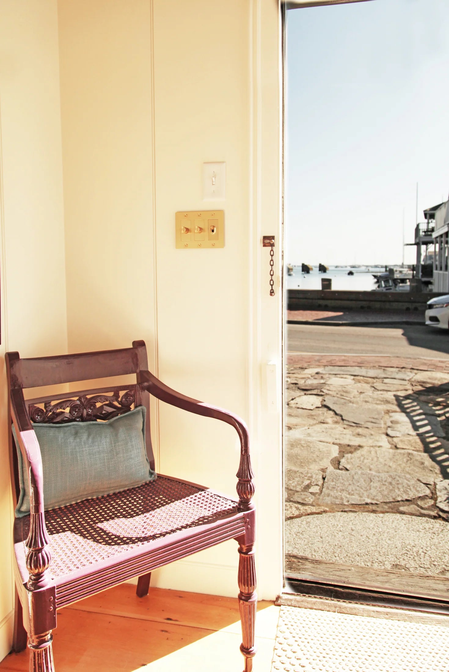 Open doorway leading to a coastal exterior with a wooden chair styled with a neutral outdoor pillow.
