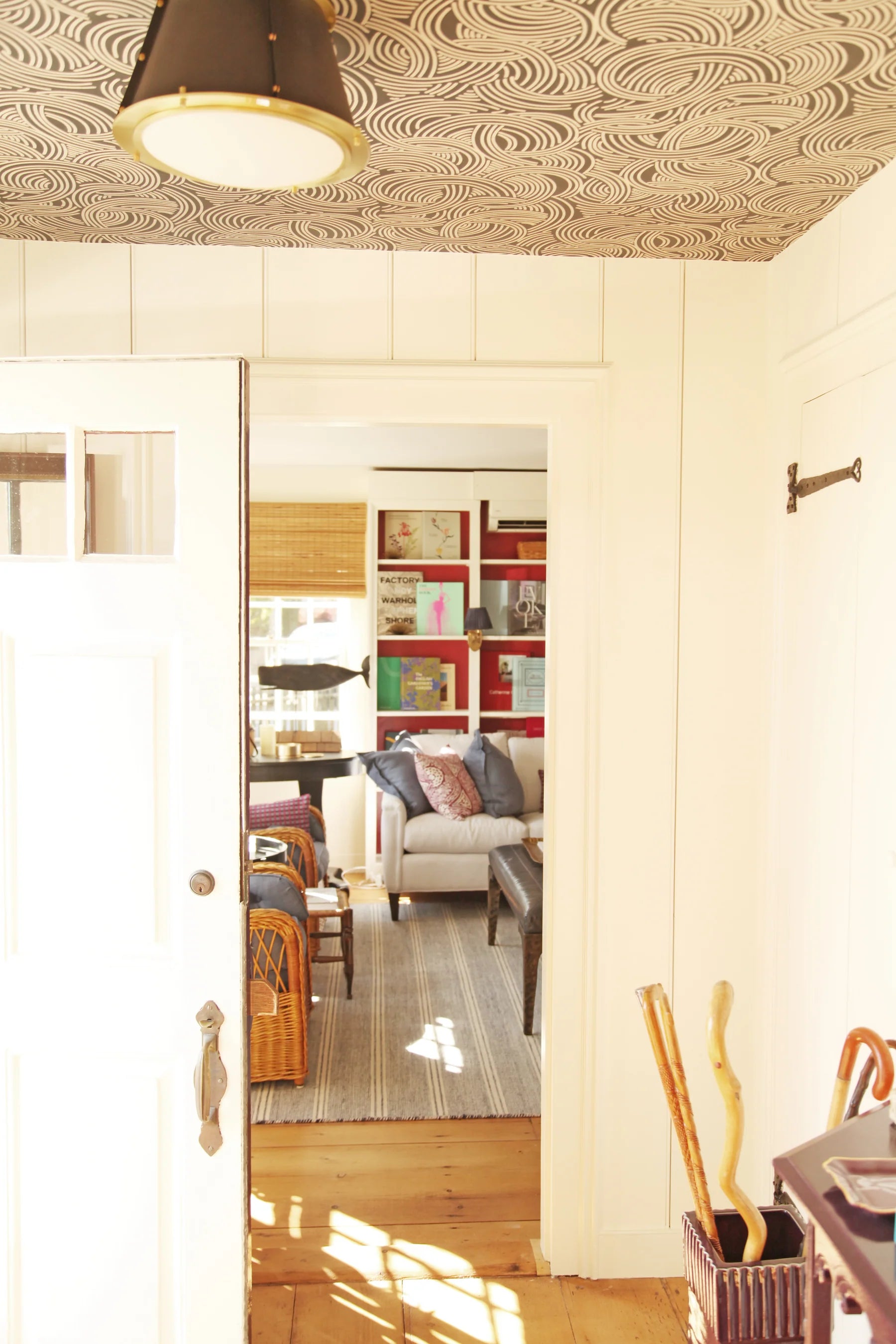 Sunlit interior view through an open door revealing layered living spaces with neutral seating and colorful accents.