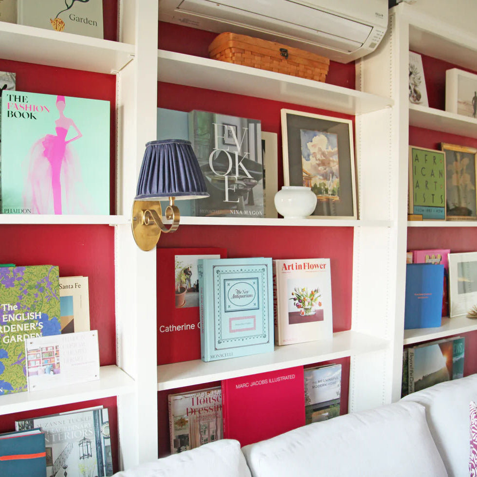 Bookshelf with books and decorative items against a red wall, with a sofa in the foreground.