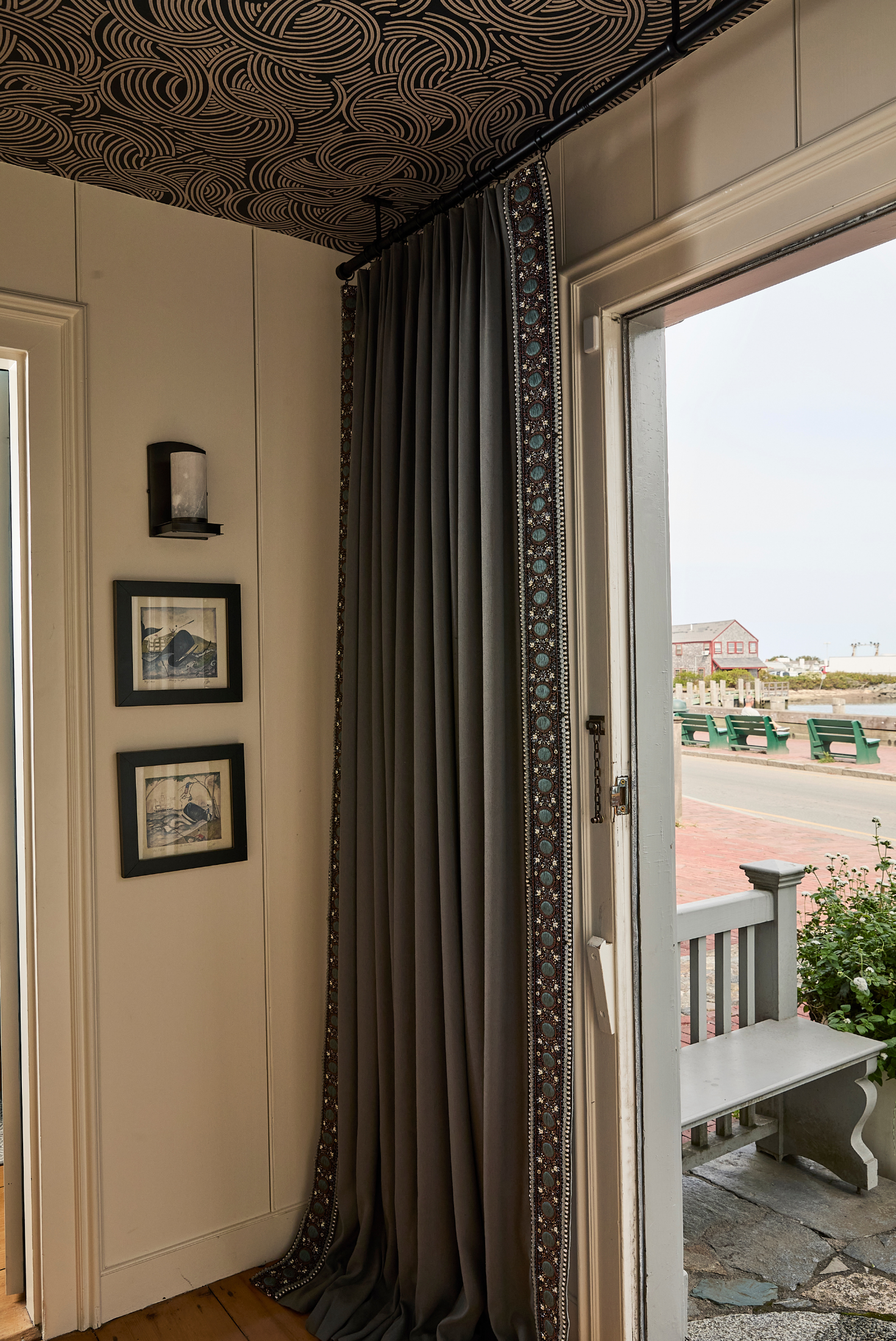 Window view of a coastal porch with drapery panels and outdoor seating visible in the distance.