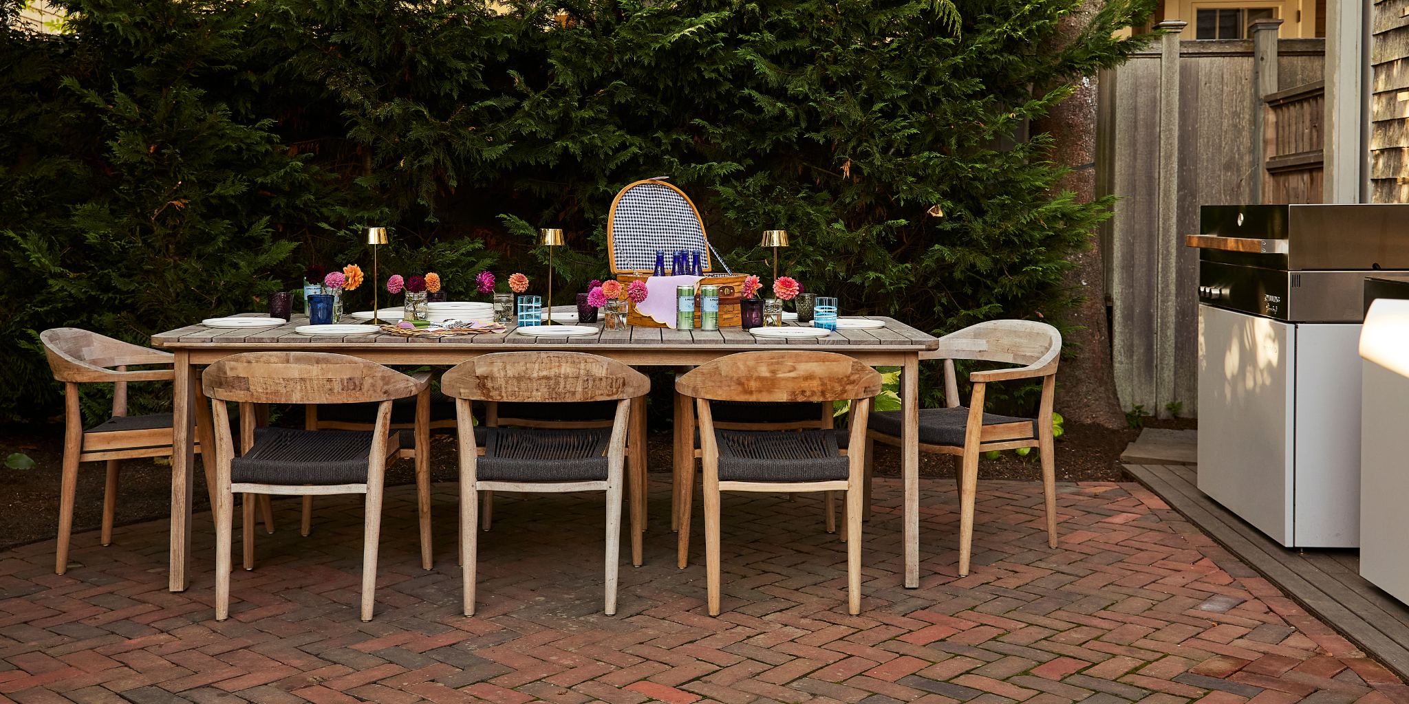 An outdoor dining table with chairs surrounding adorned with tableware
